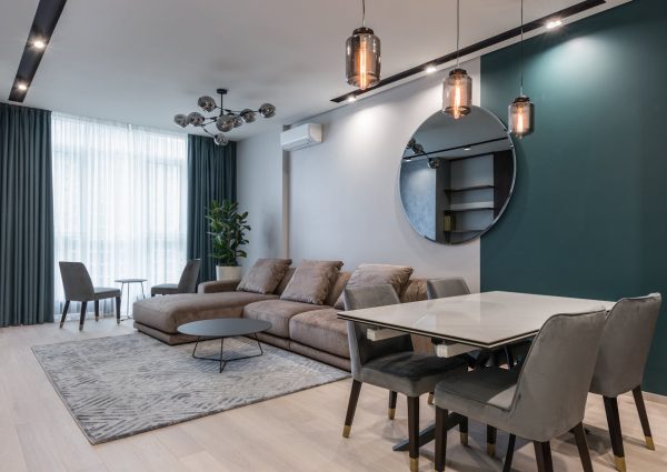 Interior of modern living room with comfortable big sofa and dining zone decorated with creative lamps and mirror in daylight
